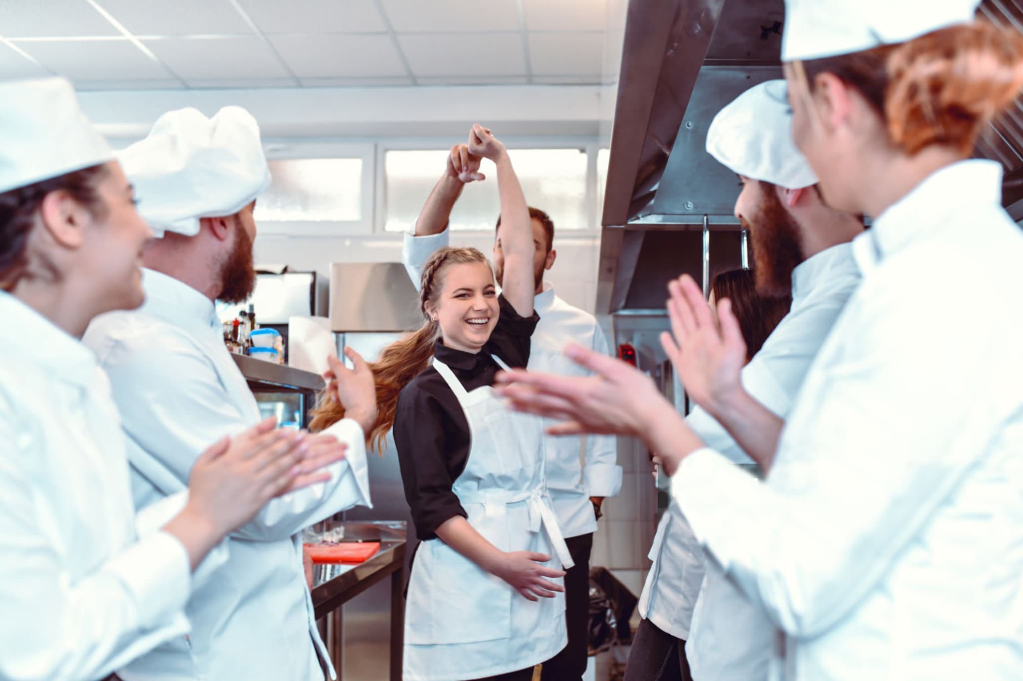 Una brigata in cucina applaude mentre una ragazza sorridente balla con un suo collega chef