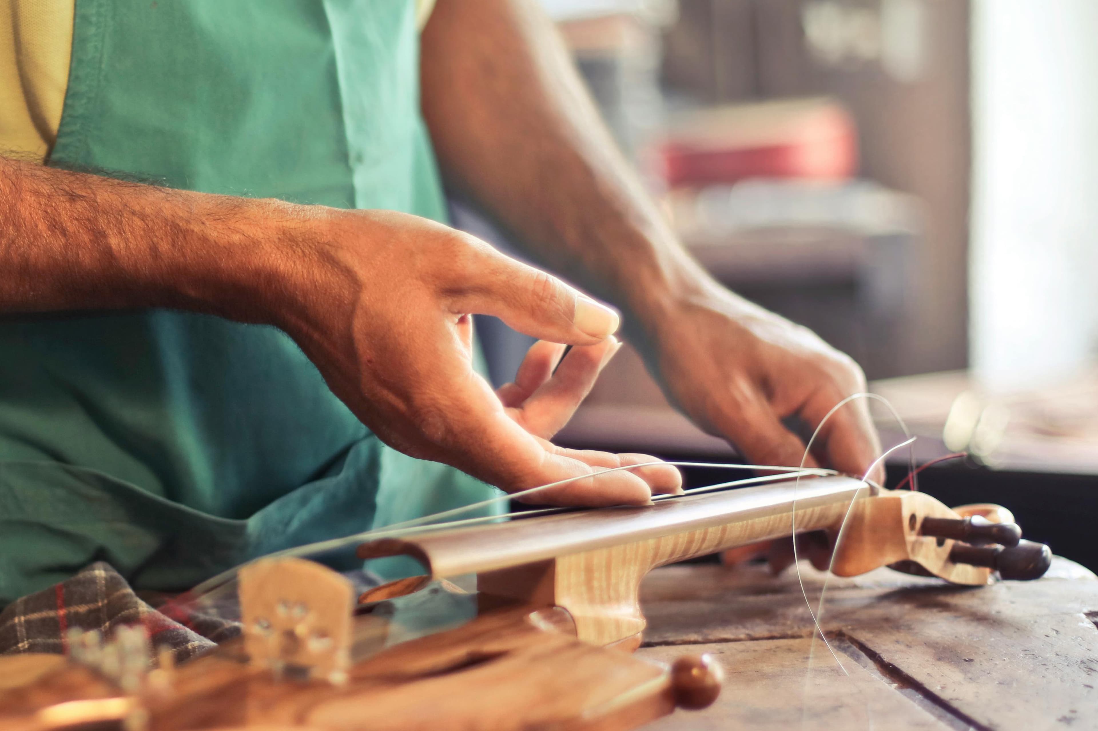 Liutaio con grembiule che lavora le corde di un violino